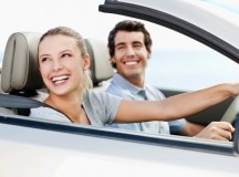 Young man and woman smile back over their shoulders while seated in a convertible car.  Horizontal shot.